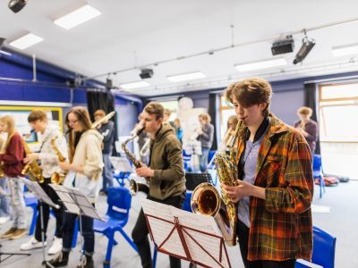 A boy in an orange checked shirt plays the saxophone. Other GYA Norwich participants are stood next to him